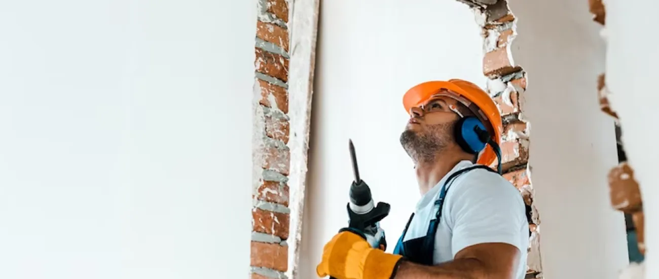 artisant avec un casque regardant un mur avant d'utiliser sa perceuse pour renover la pièce